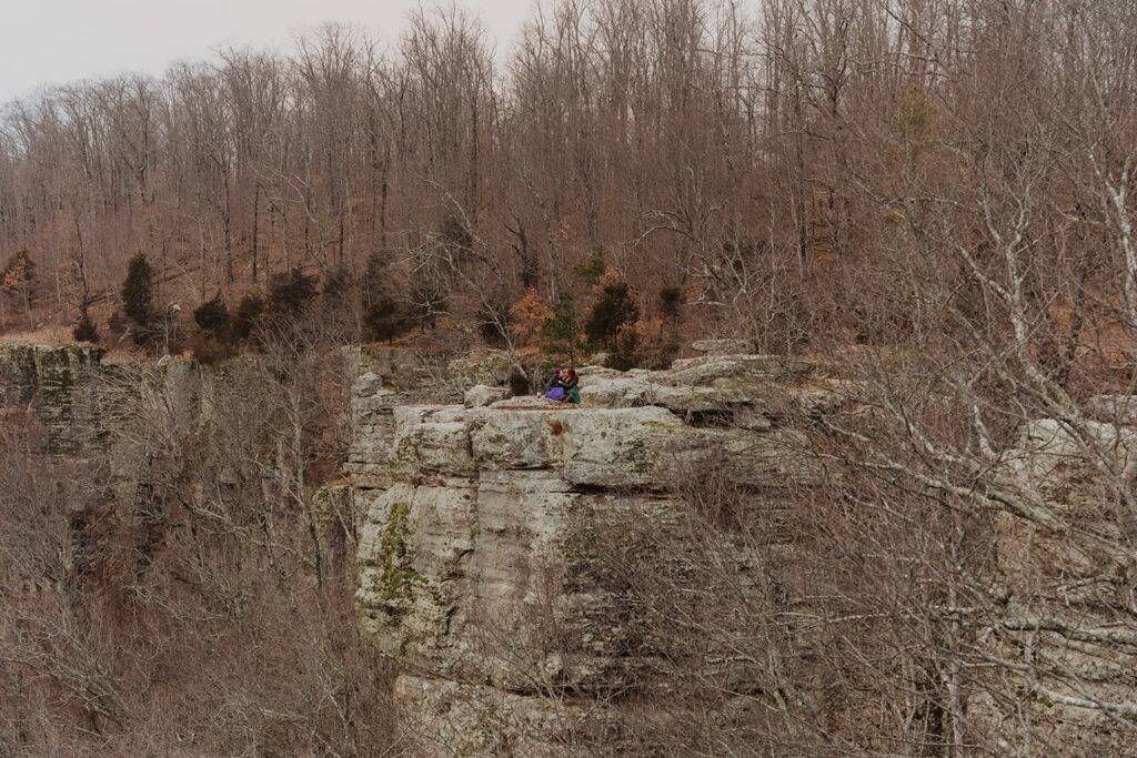 A couple is sitting on the cliff at White Rock Mountain, one of the best places to elope in Arkansas!