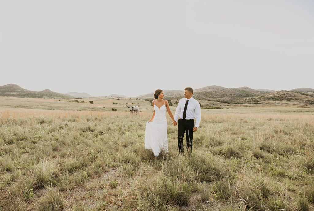 A couple standing together on their elopement day with the Wichita mountains and a bull in the background.