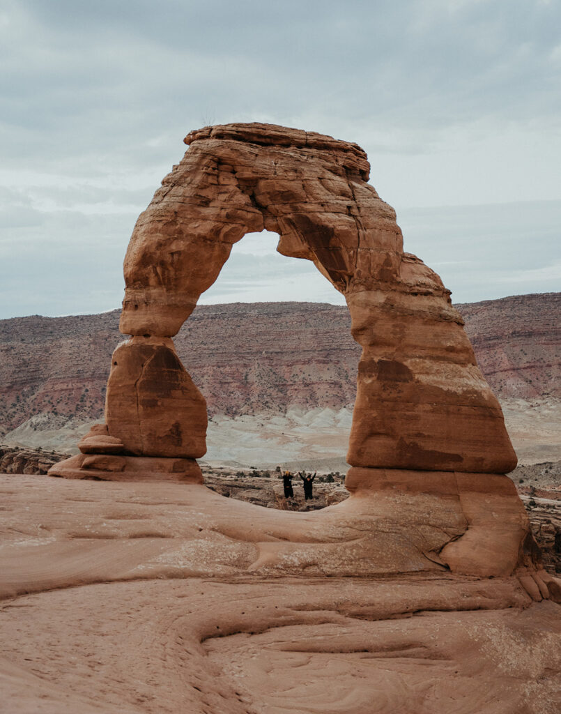 A couple jumps for a picture under a arch in arches national park