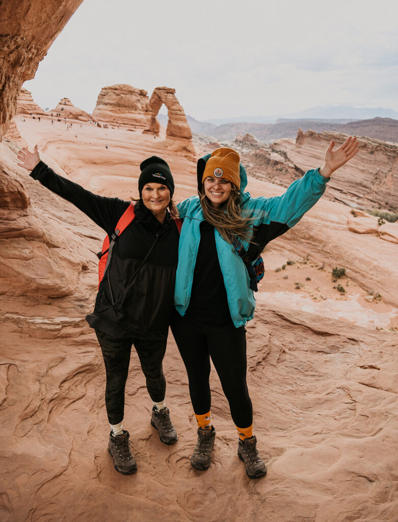 a mom and daughter pose for a picture at arches national park