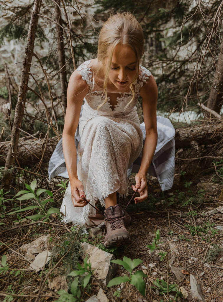 A bride in a wedding dress lacing up her hiking boots, ready to elope in a national park.