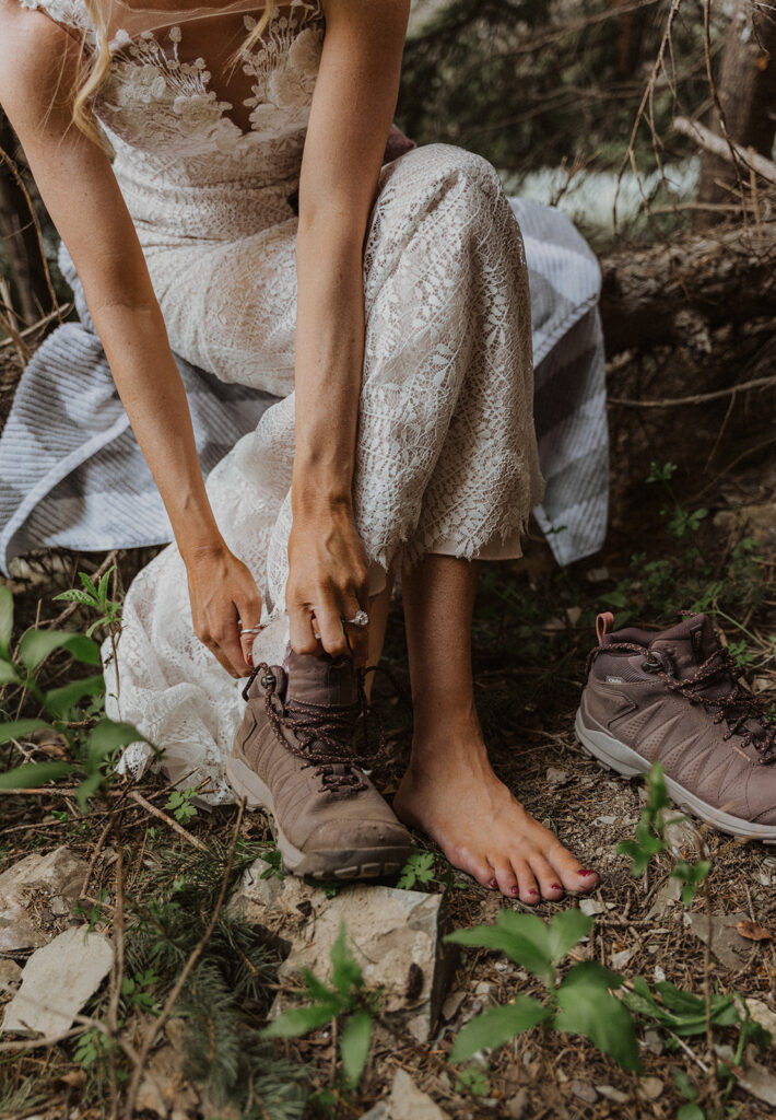 A bride putting her hiking boots on in the outdoors on her elopement day. 