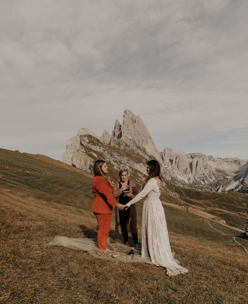 A lgbtq+ couple stands on seceda ridge line in the dolomites of italy during their elopement ceremony