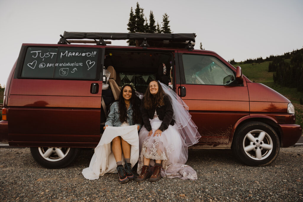 a lgbtq couple on their elopement wedding day outside of their travel van smiling.